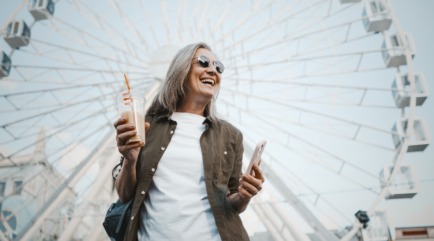 beautiful mature woman drinking smoothie by ferris wheel